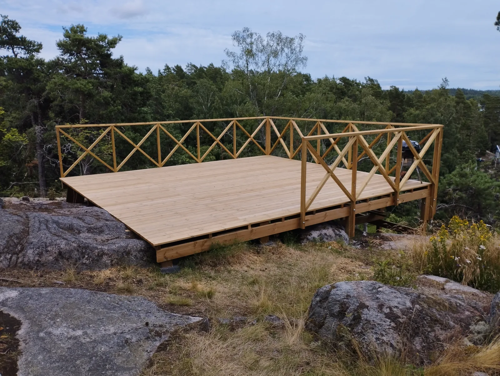 Fristående träaltan med kryssräcke på en naturtomt med berg och grönska.