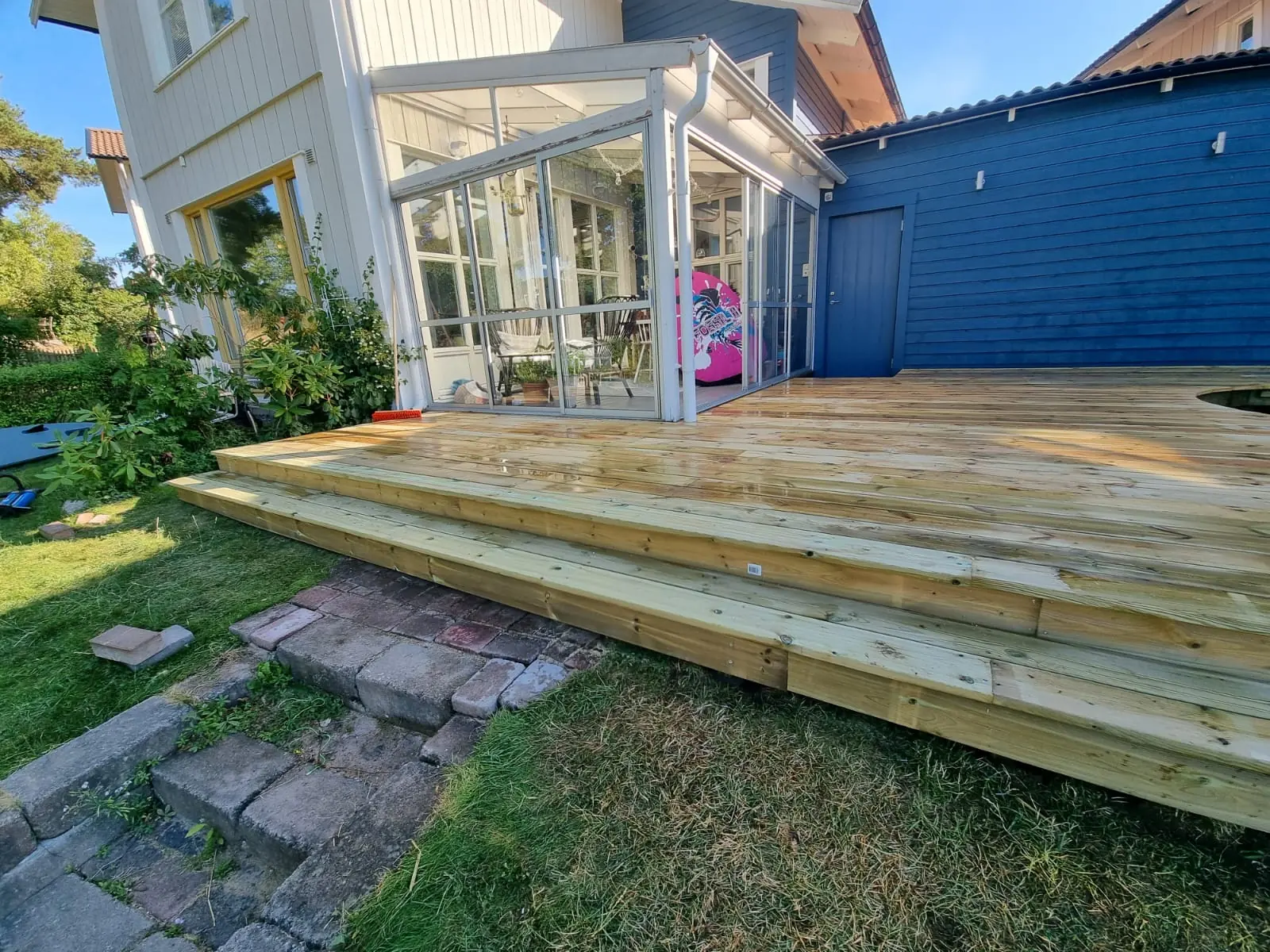 Träaltan med breda steg framför en inglasad veranda och en blå fasad i Gustavsberg.